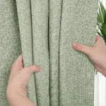 Hands holding light green linen-look curtain fabric.
