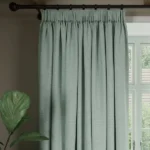 Pleated light sage soundproof curtain hangs on rod.