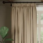 Pleated taupe soundproof curtain hangs on rod.